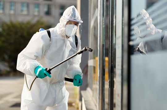 Sanitation worker in hazmat suit disinfecting public building du