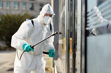 Sanitation worker in hazmat suit disinfecting public building du